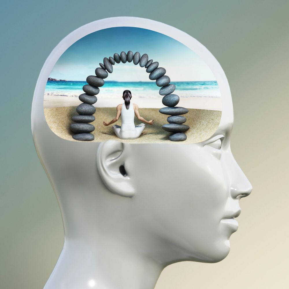 Person meditating inside a head silhouette with a stone arch on a beach.