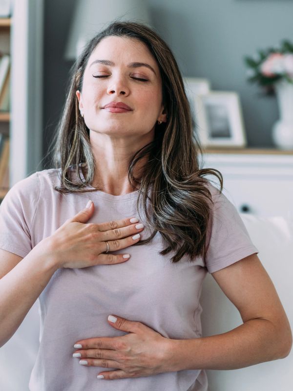 Woman practicing deep breathing with eyes closed, hands on chest and stomach.