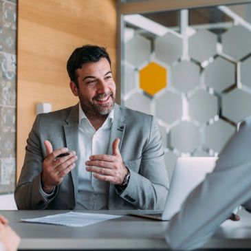 Man in gray suit talking in an office meeting.