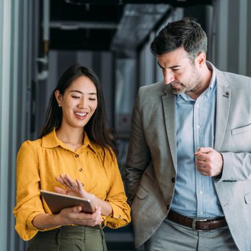 Two professionals discussing something on a tablet in an office hallway.