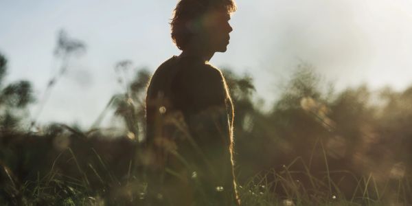 Silhouette of a person standing in tall grass during sunset.