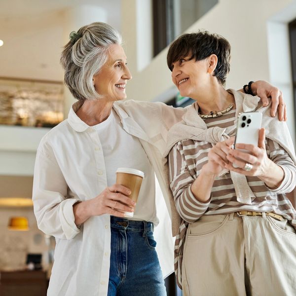 Two older women smiling and enjoying coffee together indoors.
