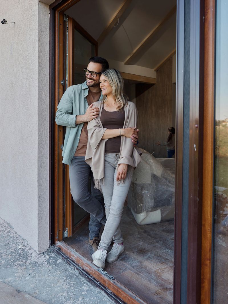Happy couple standing embraced on the door of their renovating house.