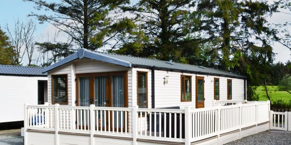 Modern mobile home with white exterior and spacious deck in a natural setting.