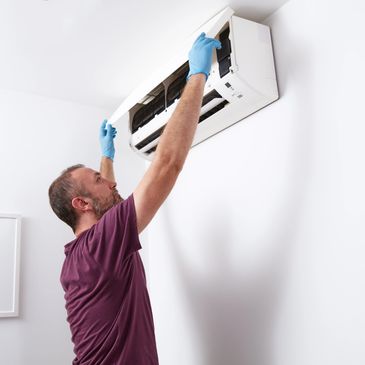 Man in gloves repairing or cleaning a wall-mounted air conditioner.