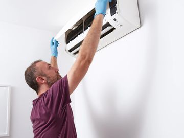 Technician repairing an indoor air conditioner unit on a white wall.