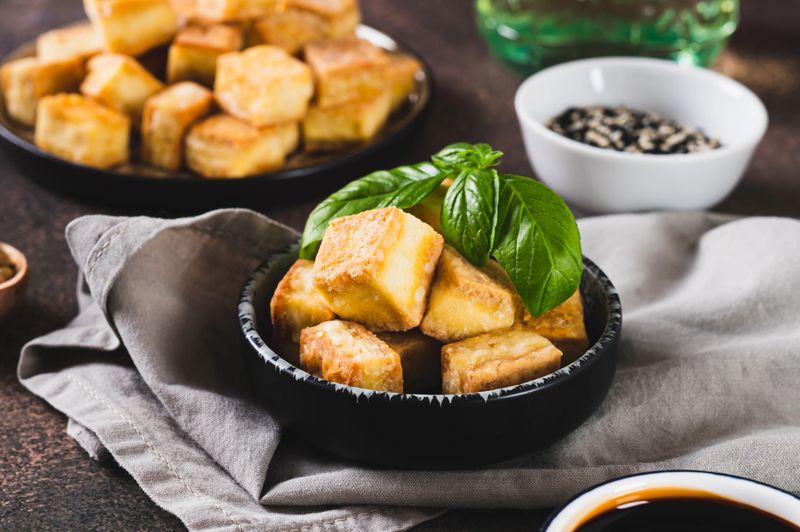 Fried vegetarian tofu cheese cubes and basil leaves in bowl on table
