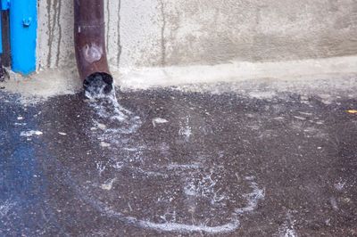 Water flowing from a drainpipe onto a wet pavement during rain.