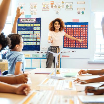 Teacher engaging students in classroom with a wind turbine model.