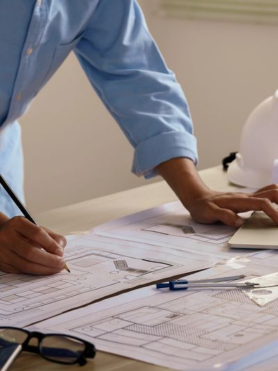 Architect working on blueprints with laptop and tools on desk.