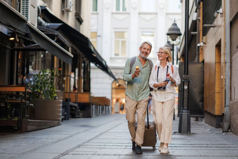 Couple enjoying a leisurely walk down a picturesque European city street, sharing an ice cream cone and laughter. Perfect for travel and lifestyle concepts.