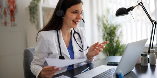 A female doctor wearing a headset conducts a virtual consultation with a laptop.