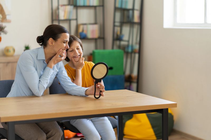 A therapist demonstrating a mouth exercise using a small mirror in speech therapy