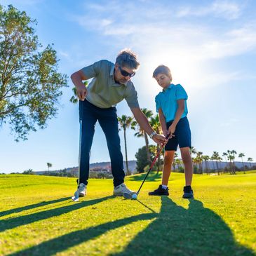Man teaching boy how to play golf on a sunny golf course.
