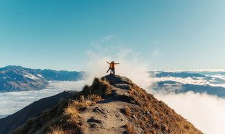 Two hikers stand triumphantly on a mountain peak above the clouds.