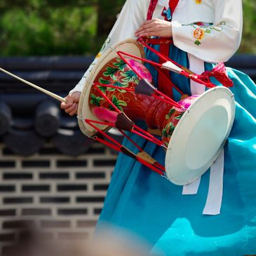 Person playing a traditional Korean drum called janggu, dressed in colorful hanbok.