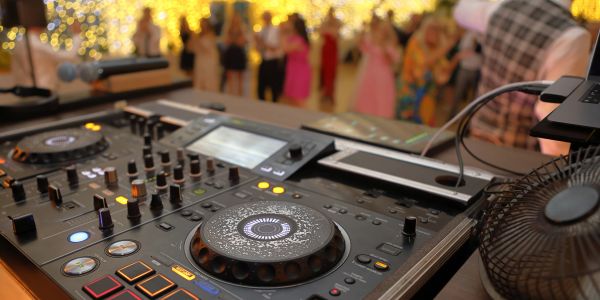DJ equipment in focus with a blurred crowd dancing at a lively party.