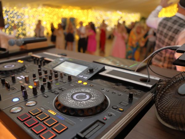 DJ equipment with party lights and dancing crowd in background.
