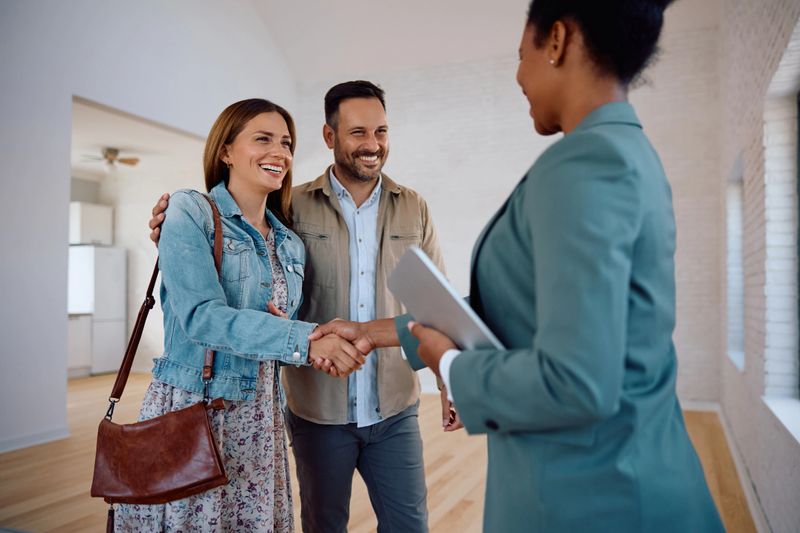 Happy woman shaking hands with real estate agent while buying new apartment with her husband.
