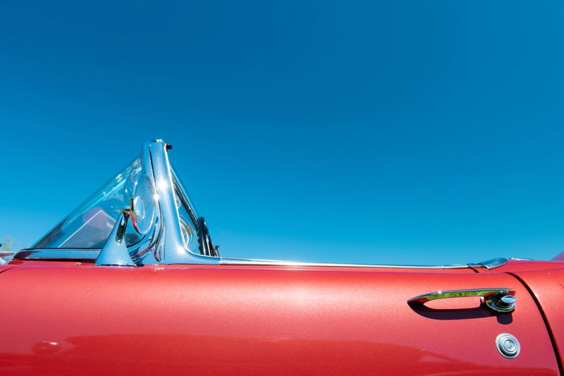 Door and windshield detail of a red convertible car with the top down under a perfect blue sky