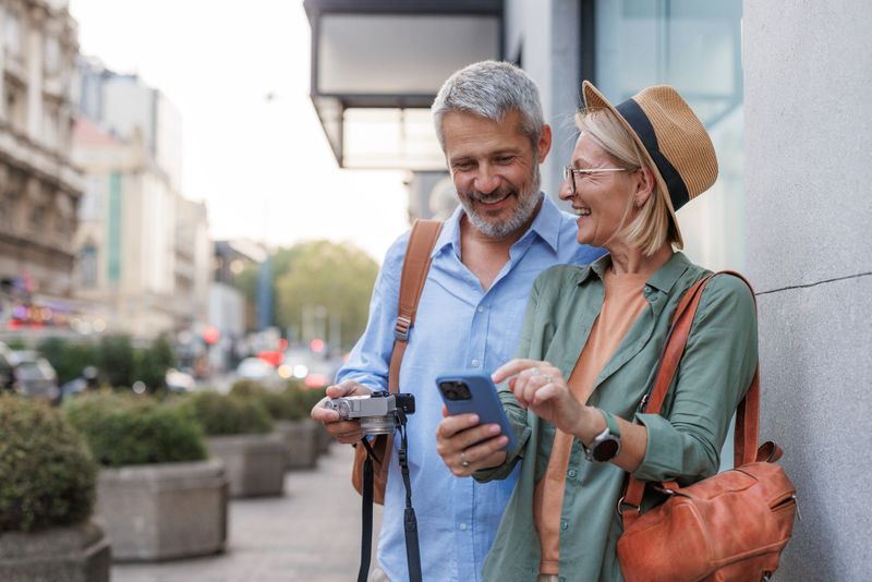 Photo of a cheerful heterosexual couple on a city break, using a phone and a camera