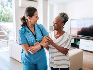 A nurse and elderly woman smiling warmly at each other indoors.