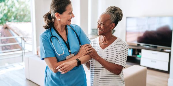 Nurse and elderly woman smiling and holding hands.