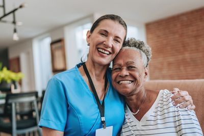 A nurse and elderly woman smiling and embracing indoors.