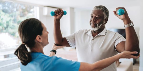 Therapist assisting elderly man with arm exercises using dumbbells.
