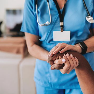 Nurse in blue scrubs comforting a patient by holding their hand.