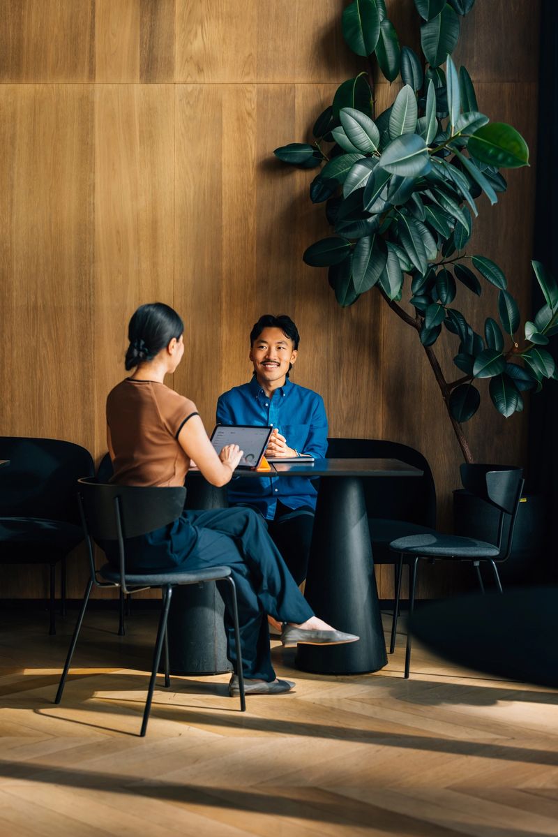 Two professionals engaged in a business meeting in a modern office setting. Natural light illuminates the scene, enhancing a calm and productive atmosphere.