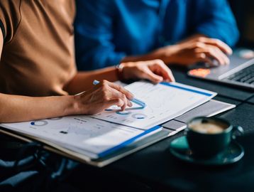 People analyzing charts and data with a laptop and coffee nearby.
