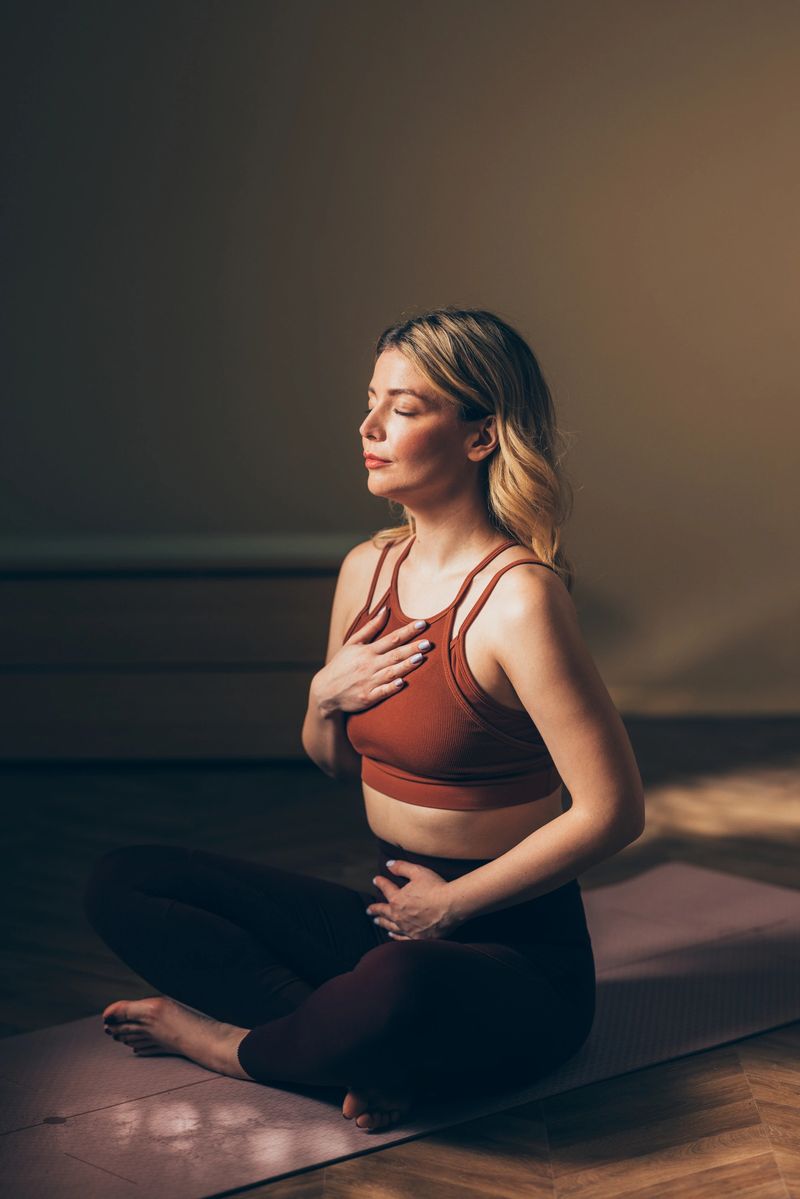 Woman sitting in a meditative pose on a yoga mat, practicing mindfulness and deep breathing in a peaceful setting.