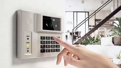 Person entering code on a home security alarm keypad inside a modern living room.