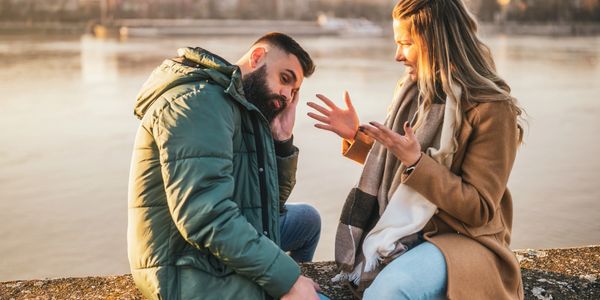 Couple having a serious conversation by the water during sunset.