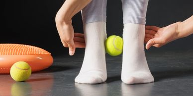 Person stretching toes with a tennis ball between feet on floor.