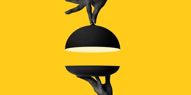 Hands holding a black serving tray and dome against a yellow background.
