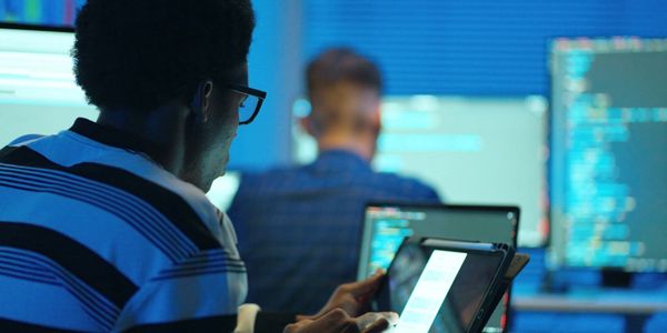 Two programmers working on coding with multiple screens and a tablet.