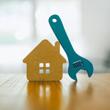 Miniature wooden house and adjustable wrench on wooden surface.