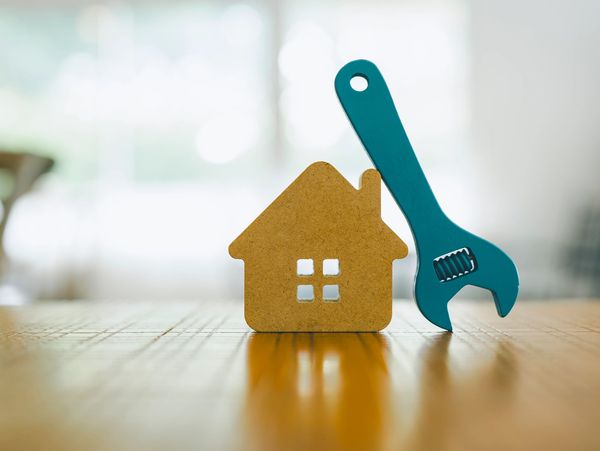 Miniature wooden house and blue wrench on wooden table.