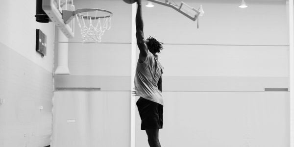 A basketball player jumps to score a slam dunk in an indoor gym.