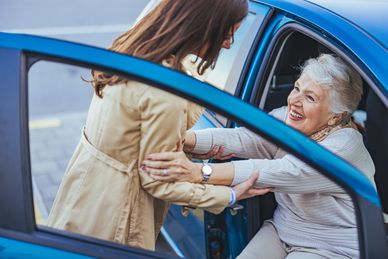 Personal support worker in Kingston, Ontario helping a smiling senior woman safely get out of a car, providing transportation assistance.