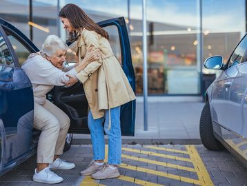 A young woman helping a senior out of a car.