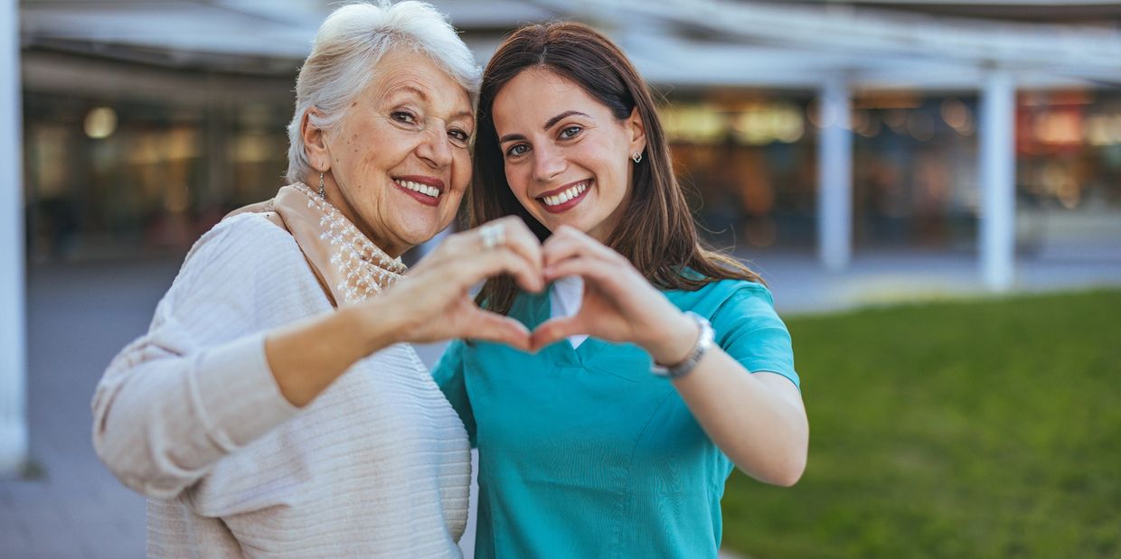 Happy client and caregiver smiling in the community, forming a heart with their hands.