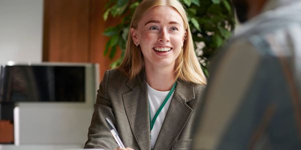 Smiling woman in a blazer engaged in a conversation while taking notes.