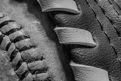 Close-up of worn baseball and leather glove stitches in black and white.
