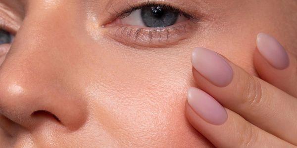 Close-up of a woman's face with natural makeup and nude almond-shaped nails.