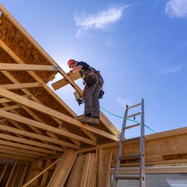 Construction worker installing a roof frame under a clear sky.