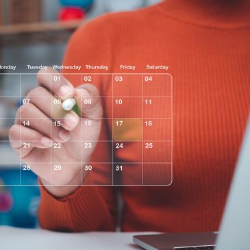 Person in orange sweater marking a digital calendar on a transparent screen.