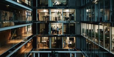 Modern office building with illuminated meeting rooms and people inside at dusk.